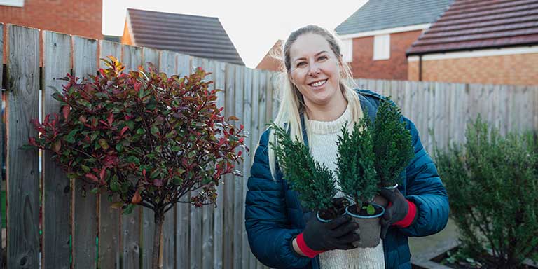 Smiling woman in a garden, holding three potted plants